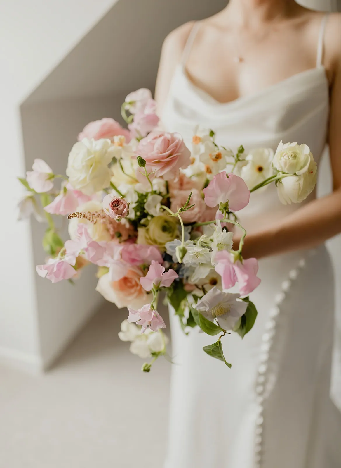 fraoch floral design bride in a white dress holding a pastel bouquet of pink and white roses, peonies, and lisianthus.