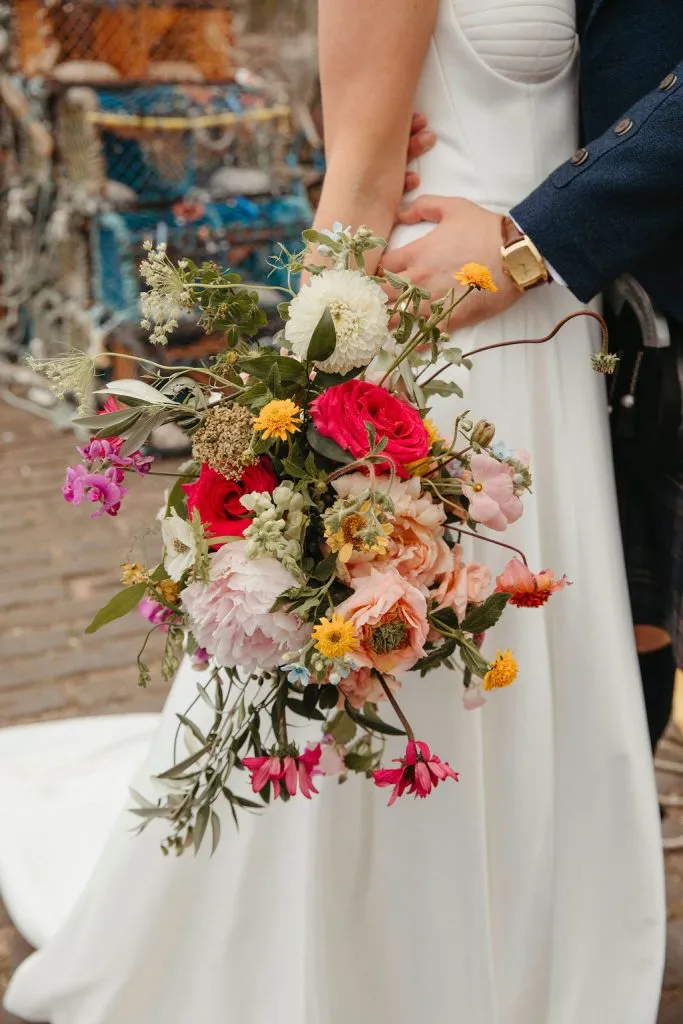 fraoch floral design bride in a white dress holds a colorful bouquet of pink, red, and yellow flowers beneath a groom0s arm in a dark suit athletic scene