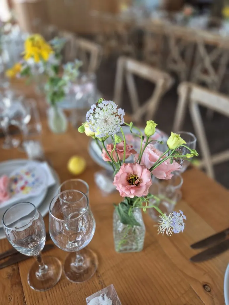 fraoch floral design close-up bouquet in a small glass vase on a wooden dining table with a blurred background of chairs and decor.