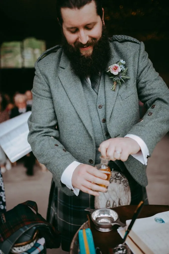 fraoch floral design bearded man in a gray suit with a boutonniere pours a drink at a wedding reception.