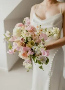 fraoch floral design bride in a white dress holding a pastel bouquet of pink and white roses, peonies, and lisianthus.