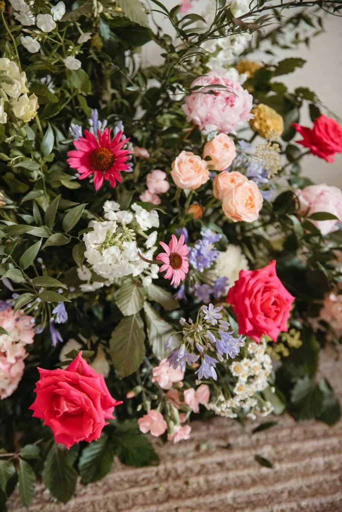fraoch floral design vibrant bouquet with pink roses, red roses, peach blossoms, white hydrangeas and purple accents among green foliage on a stone surface
