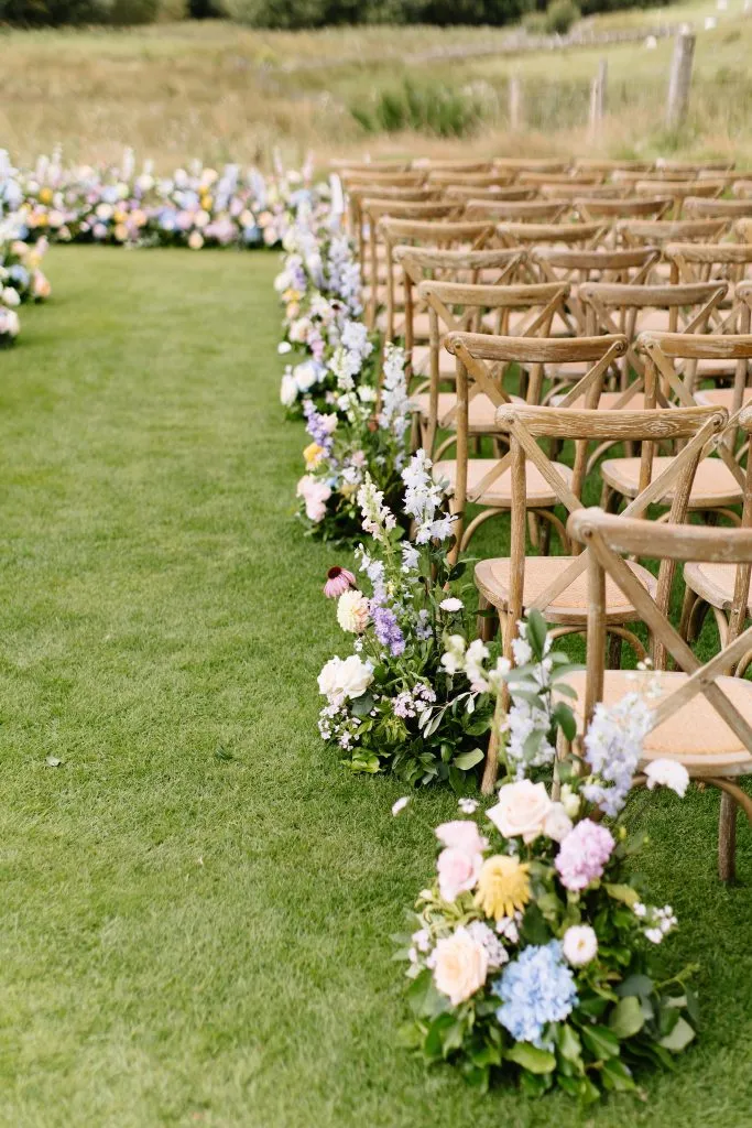 fraoch floral design outdoor wedding ceremony setup with wooden chairs outlining a flower-adorned aisle on green grass