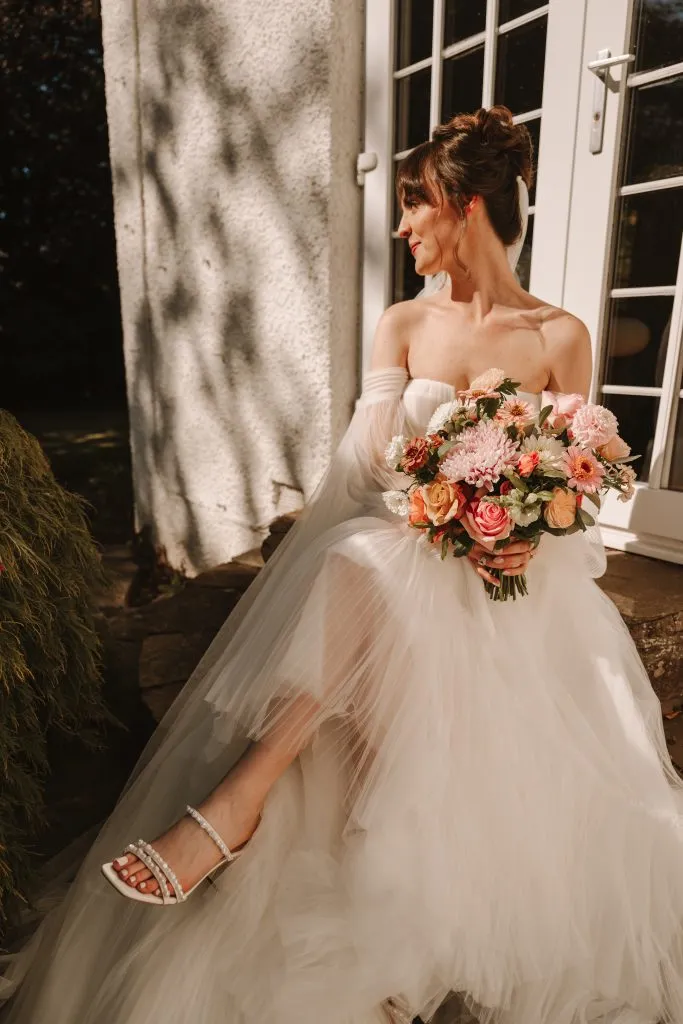 fraoch floral design bride in a strapless wedding gown holding a pink bouquet, standing beside a white door outdoors.