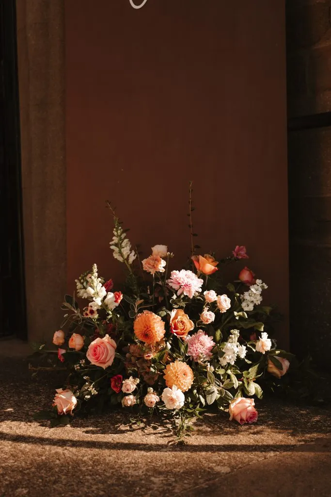 fraoch floral design colorful bouquet of pink, peach, and white flowers resting at the base of a tall brown panel