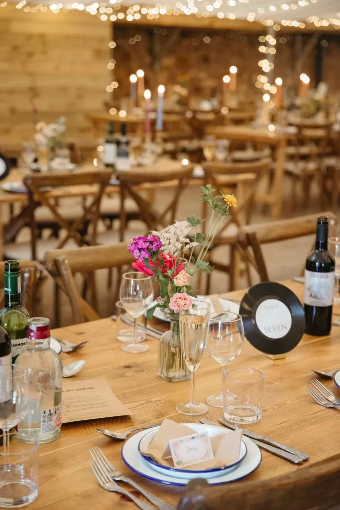 fraoch floral design wooden table set for a formal dinner with a glass vase of colorful flowers, candles, wine bottles, and neatly arranged place settings.