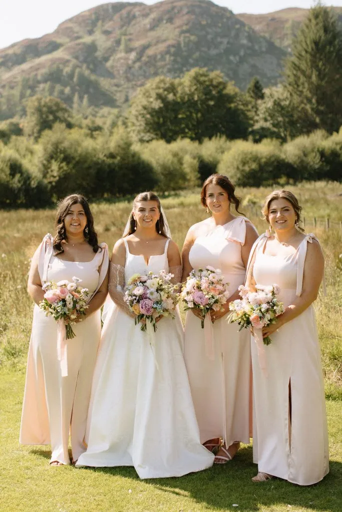 fraoch floral design four bridesmaids in pale pink dresses holding bouquets outdoors, with hills and trees in the background.